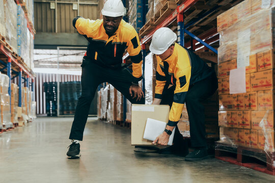 Male coworker assists black coworker who is lifting boxes and has back injury : Friendship during work and concern for safety and health while lifting heavy boxes in the warehouse.