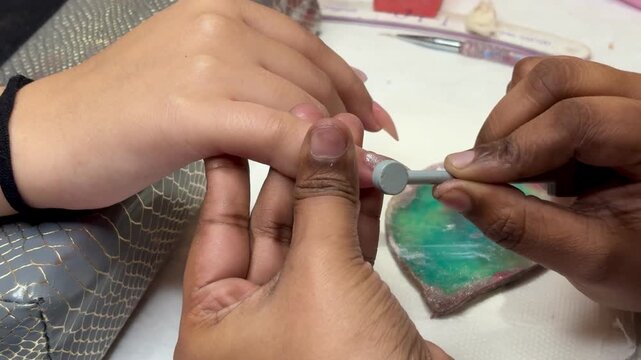 Close-up of nail technician creating magnetic nail art design using magnet tool on gel polish for unique cat eye effect in a professional salon.