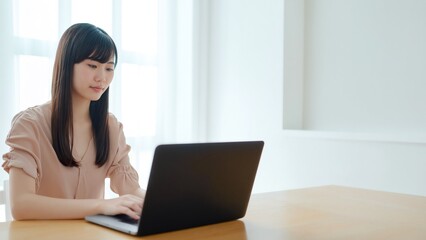 窓際でノートパソコン作業をする女性のテレワーク風景