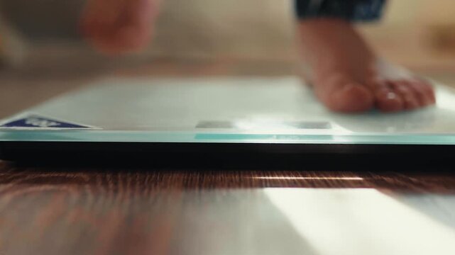 Close-up of male bare feet stepping on digital scales to check weight.