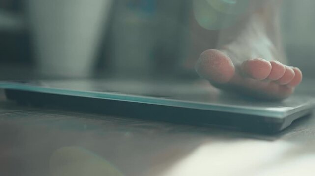 Close-up of male bare feet stepping on digital scales to check weight.