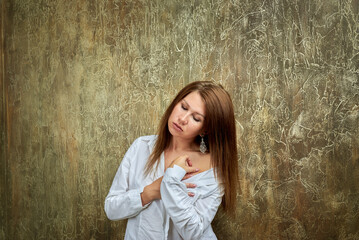 Fototapeta premium Sexy young woman in a white shirt is depicted on a textured brown background. Her long straight hair has a brownish tint.