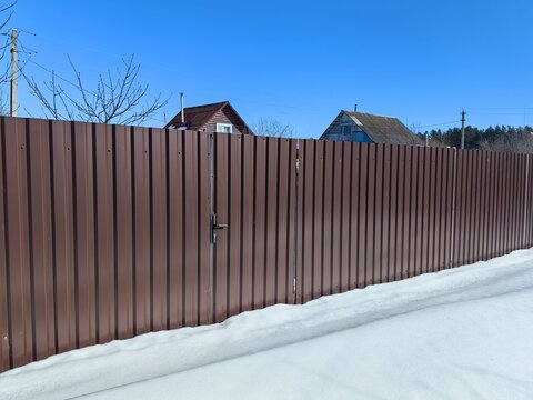 A fence at the dacha in the winter with snow, metal gates with a wicket.