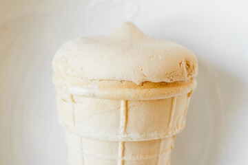 Creamy frozen dessert in a light waffle cone, positioned upright in a clean white bowl, ready to be...