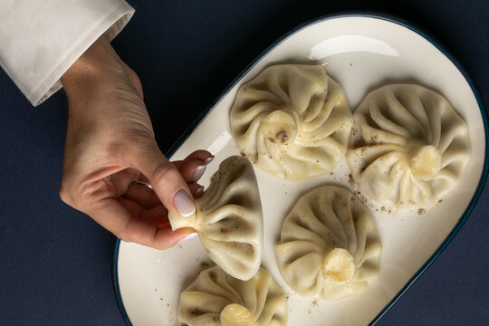 A hand elegantly lifts a steaming khinkali from a plate, exuding fragrant spices of Georgian Orthodox feast day
