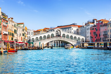 Famous Rialto Bridge spanning the Grand Canal in Venice, Italy, surrounded by historic colorful buildings and turquoise water under clear blue sky.  © preto_perola