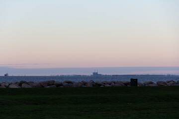 Industrial skyline over sea at dusk with rocky coastline