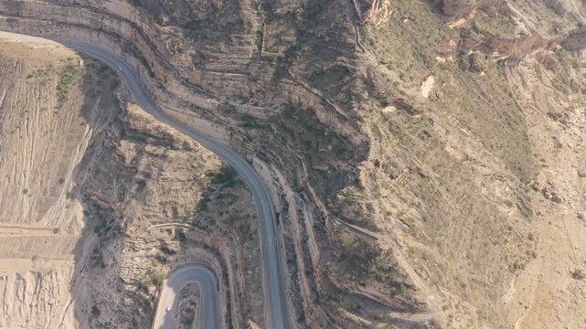 Aerial view of a winding mountain road with hairpin turns and cars traveling through steep rocky cliffs in the mountains of Iran.