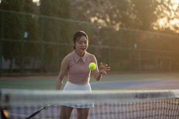 Active Asian woman player hitting a ball with a racket during a match on an outdoor tennis court, sports and healthy lifestyle concept