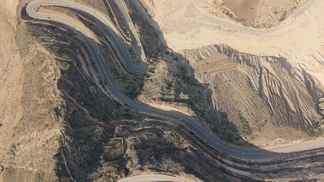 Aerial view of vehicles traveling along a winding mountain road with sharp hairpin turns through an arid landscape in Iran.