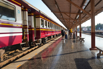 Obraz premium The daytime atmosphere at the train station, with a train parked on the platform as passengers and travelers carrying luggage walk along the station.
