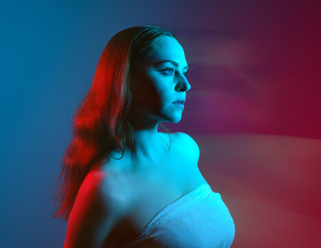 Close up studio portrait of female model face with creative neon studio lighting and slow shutter speed creating colourful blue and red 3d surreal effect.