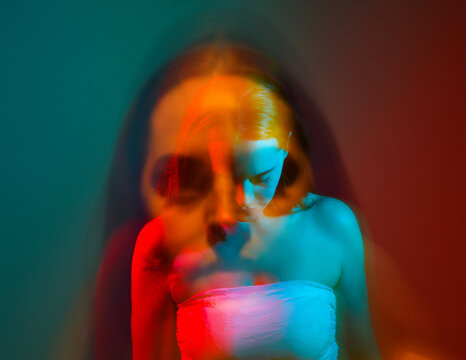 Close up studio portrait of female model face with creative neon studio lighting and slow shutter speed creating colourful blue and red 3d surreal effect.