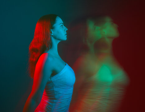 Close up studio portrait of female model face with creative neon studio lighting and slow shutter speed creating colourful blue and red 3d surreal effect.