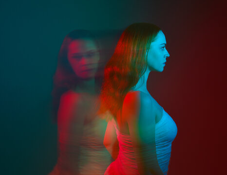 Close up studio portrait of female model face with creative neon studio lighting and slow shutter speed creating colourful blue and red 3d surreal effect.