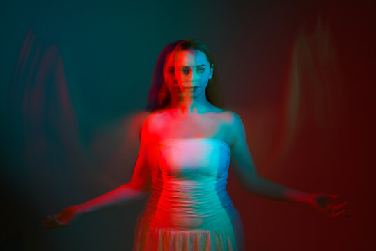 Close up studio portrait of female model face with creative neon studio lighting and slow shutter speed creating colourful blue and red 3d surreal effect.