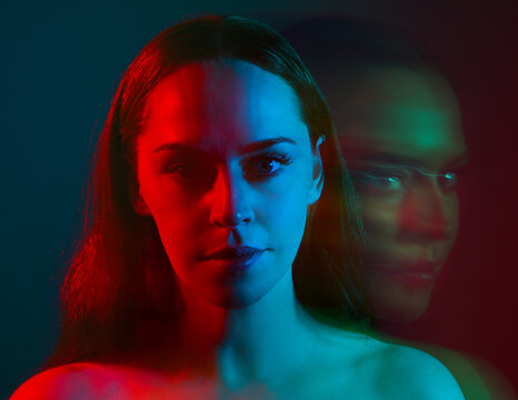 Close up studio portrait of female model face with creative neon studio lighting and slow shutter speed creating colourful blue and red 3d surreal effect.