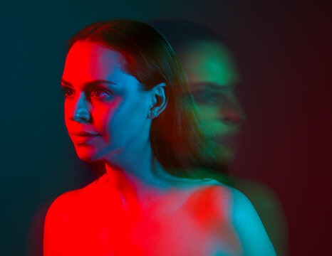 Close up studio portrait of female model face with creative neon studio lighting and slow shutter speed creating colourful blue and red 3d surreal effect.