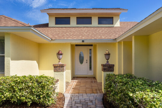 Exterior entry courtyard to yellow house with carriage lights and bushes in Florida