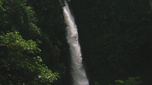 Tropical waterfall cascading into a rocky river stream surrounded by a lush green forest in East Java, Indonesia
