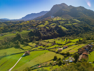 Naklejka premium Epic green mountain valley panorama. Cinematic aerial drone view of rural farmland and Picos de Europa mountains in Asturias, Spain. 