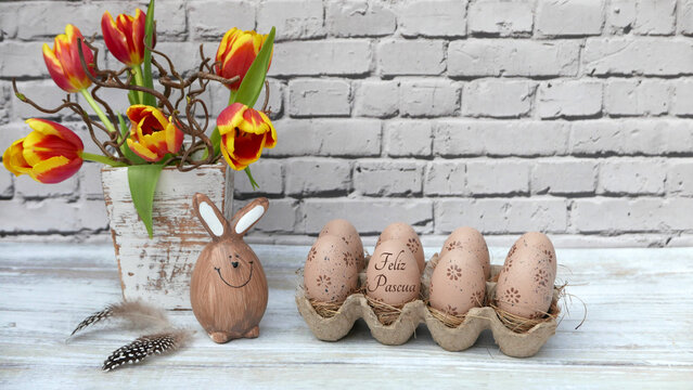 Felices Pascuas. Ramo de flores con conejito de Pascua y huevos marrones. Uno de los huevos lleva la inscripci&oacute;n "Felices Pascuas".