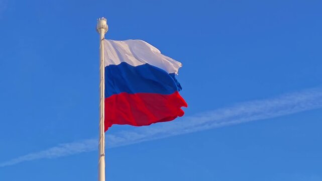 A bright sky serves as the perfect backdrop for the tricolor Russian flag waving gracefully on a flagpole. Patriotic and symbolic.