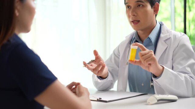 Asian male doctor explaining medication dosage to a female patient during a clinic consultation.