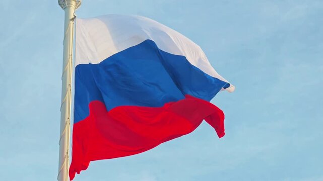 A bright sky serves as the perfect backdrop for the tricolor Russian flag waving gracefully on a flagpole. Patriotic and symbolic.
