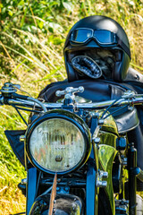 Fototapeta premium Classic motorcycle resting in a grassy field with a helmeted rider figure on a sunny afternoon