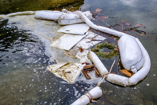 Oil containment booms are used to manage water pollution in a lake during winter near a small town in the background with mountains visible