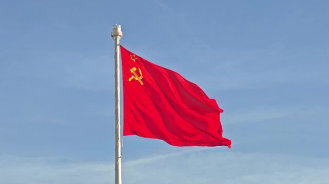 The red flag of the Union of Soviet Socialist Republics waves in the wind against a sky background. Historical communist symbol and USSR heritage.