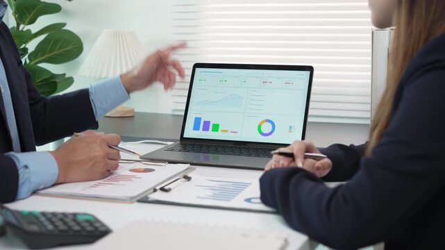 Business professionals analyzing financial data on a laptop and printed charts during an office meeting