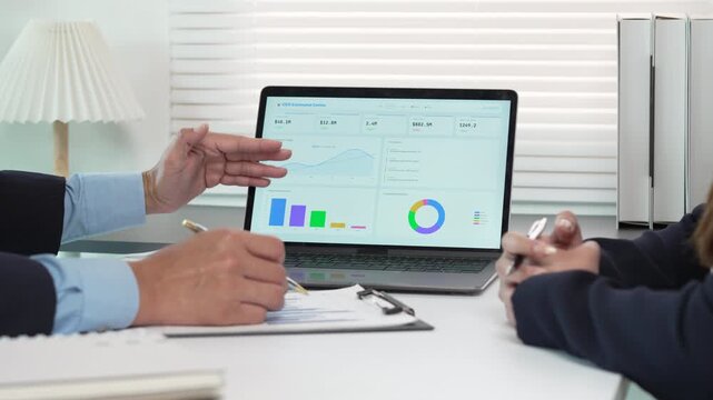 Business professionals analyzing financial growth data on a laptop screen and printed reports in a modern office