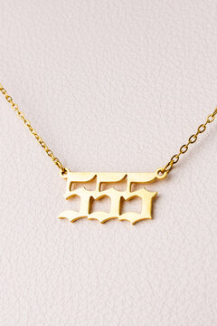 Close-up of a gold pendant with the number 555 on a chain, set against a luxurious white leather background.
