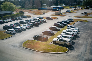 Wide overhead scene of a sunlit parking lot with rows of vehicles, curved medians and access roads, useful for themes of commuting, traffic and land use © K