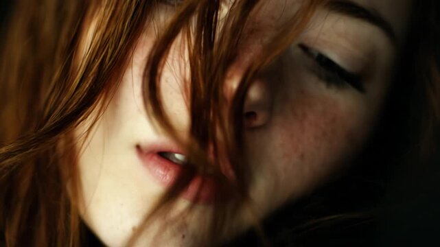 Close-up portrait of a young woman with striking red hair and freckles against a dark background