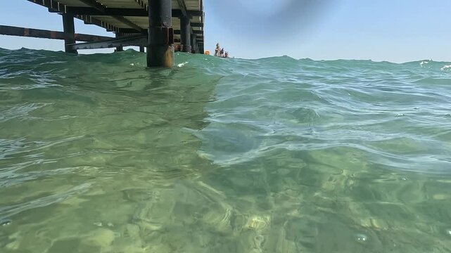 Clear sea water flowing under a wooden jetty in the Sinai Peninsula. Tropical summer travel destination with turquoise waves and sunlight on the ocean surface.