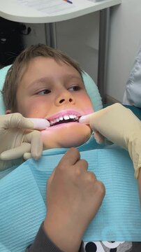 Caucasian boy receiving removable bite plate, orthodontist fitting in bright dental clinic gloved hands position purple thermoplastic plate, dental