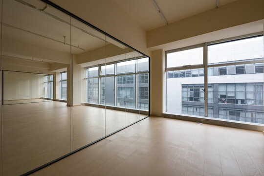 Spacious dance studio with mirrored wall, wooden floor, large windows and natural lighting