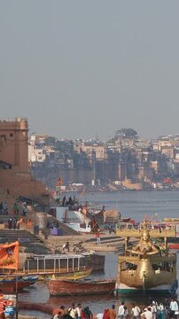 Varanasi, India. View On Ganga Mahal Ghat. Boats Moored On Ganga River Near Lassi Ghat And Tulsi Ghat. Gold Richly Decorated Pleasure Boat With Statue Of Ganga Goddess In Front For River Ride. Family