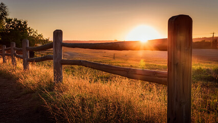 Fototapeta premium Sunrise and sunset over a peaceful countryside fence with sky and clouds