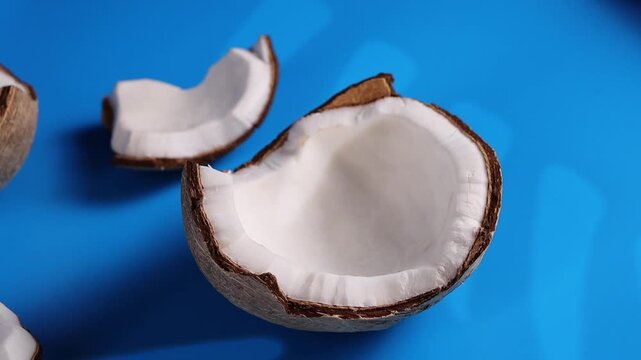 Coconut pieces on blue background with green leaves under bright light showcase tropical fun, food styling concept for creative advertising and social media visuals