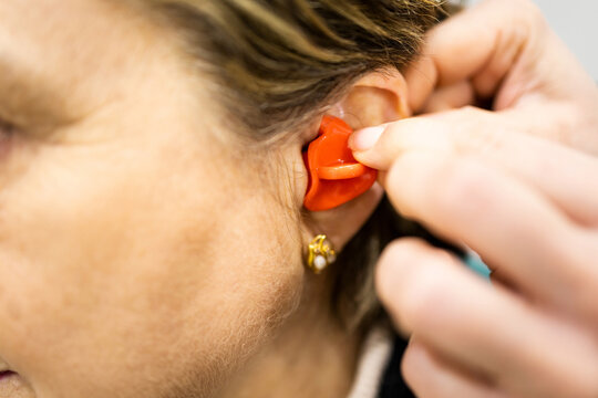Close-up photograph of an ENT specialist inserting a custom-made silicone earplug into an elderly woman. Concept of custom-made earplugs in a medical clinic.