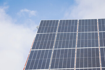 Naklejka premium Solar panels stand tall against a backdrop of soft clouds and a vibrant blue sky. This scene captures the essence of renewable energy shining brightly in the afternoon sun