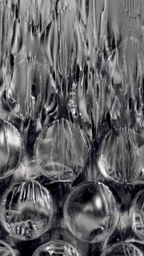 Black and white macro view of a sheet of bubble wrap plastic melting under heat, with the bubbles popping, the material shriveling, stretching, and finally disappearing into the dark background