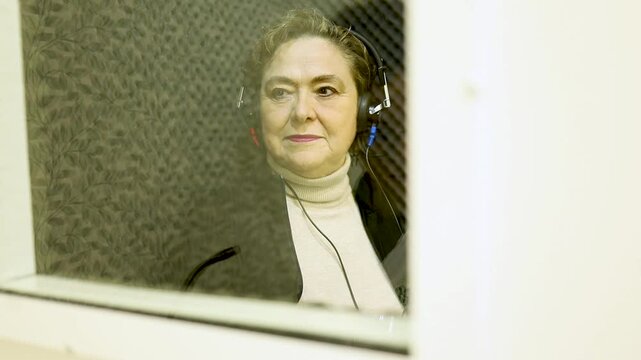 Video of a 60-year-old woman undergoing hearing tests at a medical center. The test is conducted in a soundproof booth. Upon hearing the sound, she raises her hand through the glass.