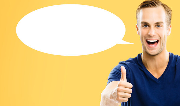 Portrait image - happy smile young man wear blue t shirt cloth shows points thumb up thumbup finger hand sign, isolated orange yellow background. White empty speech bubble speechbubble. Right choice