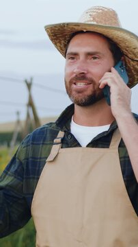 Portrait of modern agronomist man has conversation with business partners or clients in a field at sunset. Businessman talking on the phone near the wheat field. Professional male farmer talking