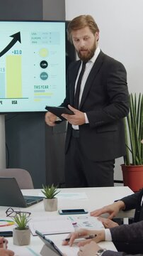 Good-looking confident high-skilled bearded expert representing business strategy on interactive screen during seminar with attantive multiracial listeners in boardroom,close up
